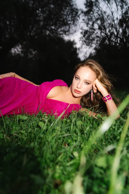 Modella con abito fucsia sdraiata sull’erba, fotografata con il flash