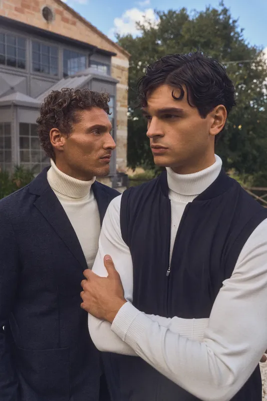 Due modelli in dolcevita bianco e giacca blu davanti a una villa di campagna