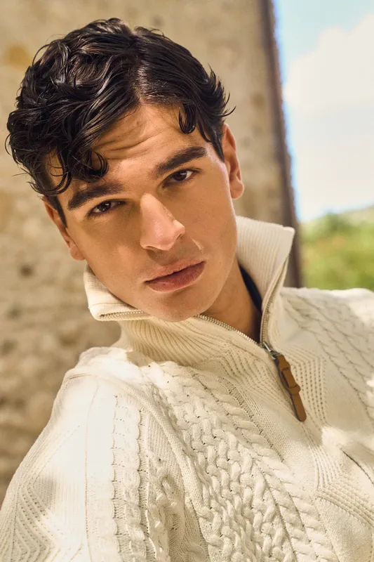 Primo piano di un ragazzo con maglione a trecce color crema con zip
