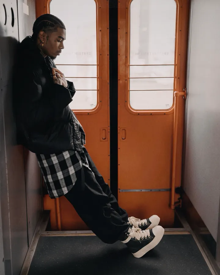 Ragazzo appoggiato alla porta di un vagone del treno, con sneakers alte