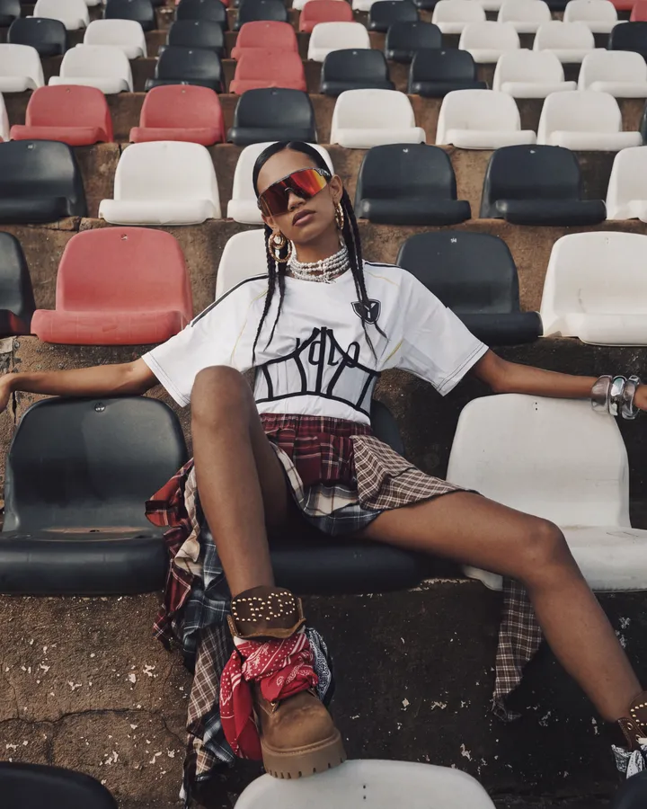Ragazza seduta sulle gradinate di uno stadio con stivali e gonna scozzese