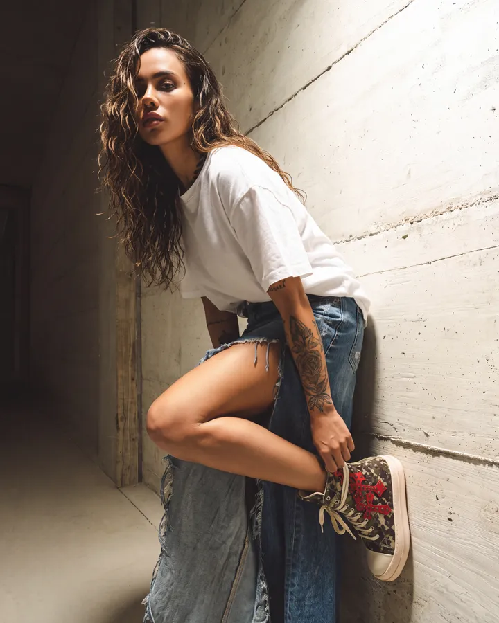 Ragazza con jeans e t-shirt bianca appoggiata a un muro, con sneakers alte
