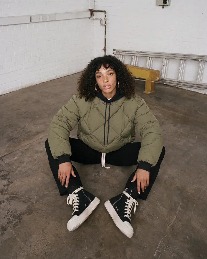Ragazza seduta a terra con piumino verde oliva e sneakers alte nere