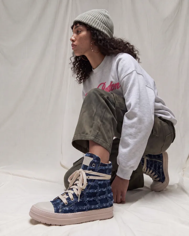 Ragazza accovacciata con pantaloni cargo, felpa grigia e sneakers in denim