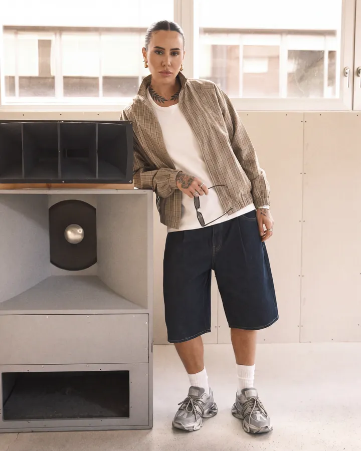 Ragazza con giacca beige e shorts di jeans accanto a grandi casse audio