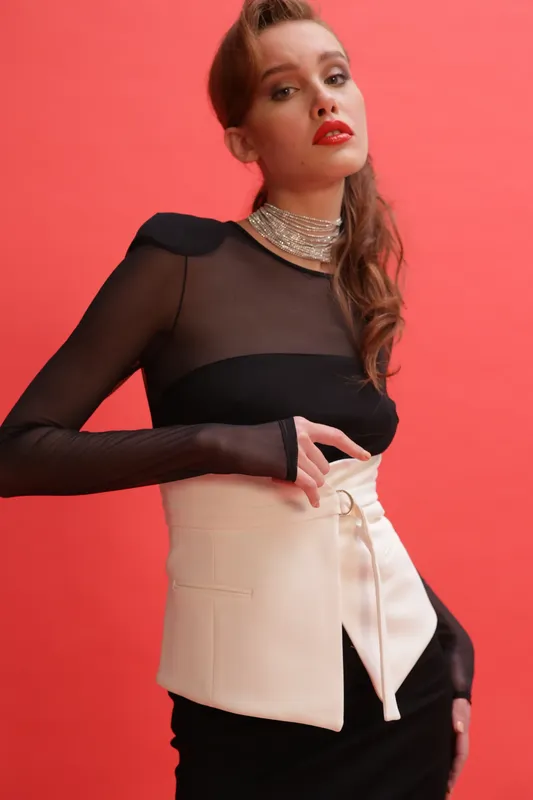 Modella con top nero trasparente e corsetto bianco su fondo rosso