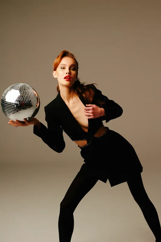 Modella con blazer nero che tiene una palla da discoteca