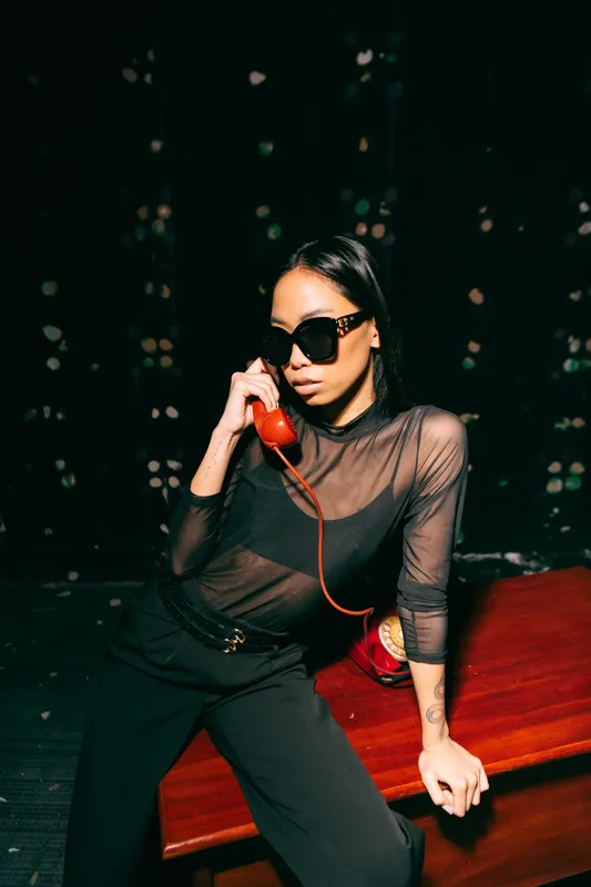Donna con occhiali da sole al telefono con una cornetta rossa, su fondo scuro con brillanti